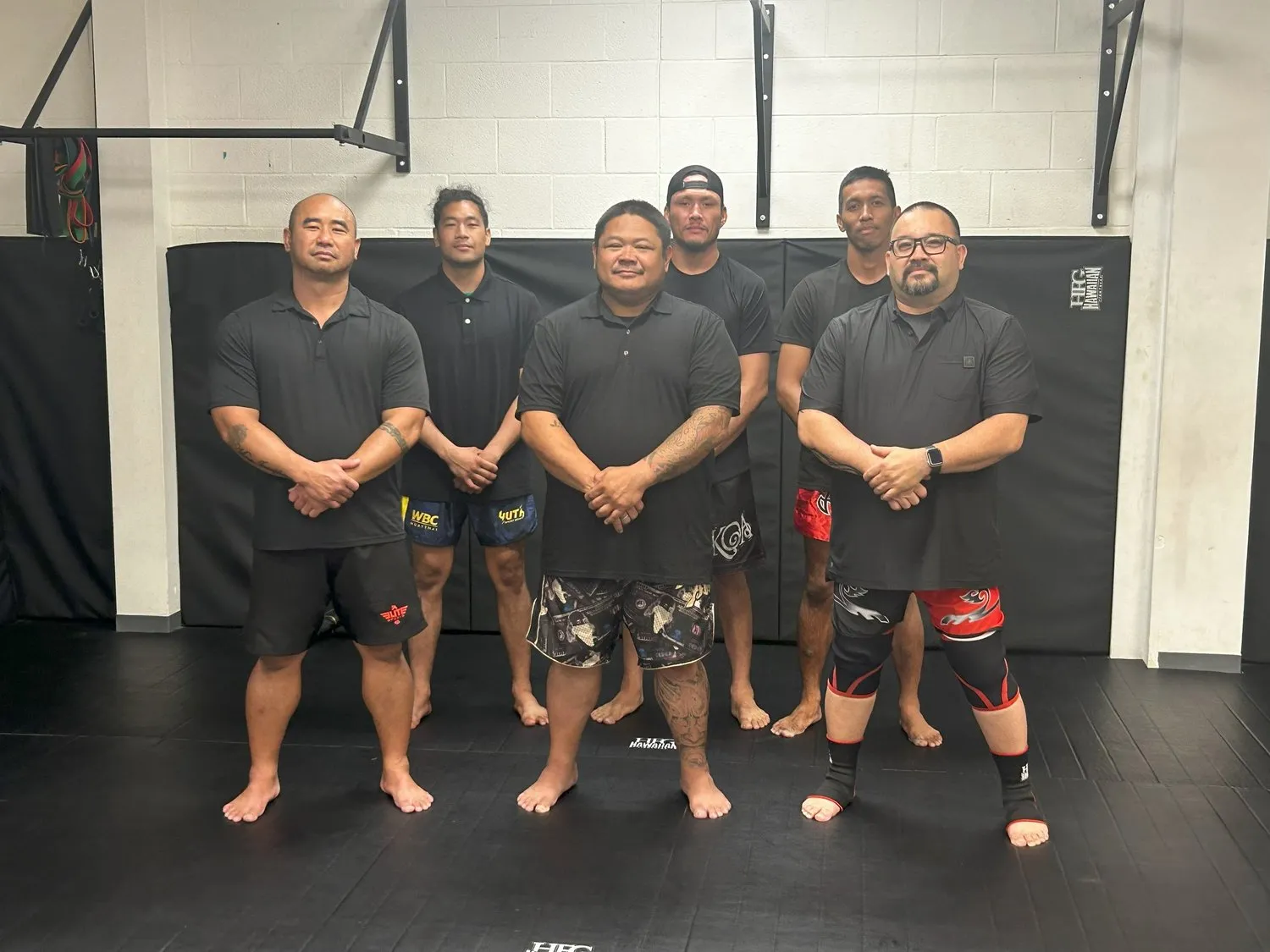 The Iron Kingz coaching team standing together in black shirts on the mats