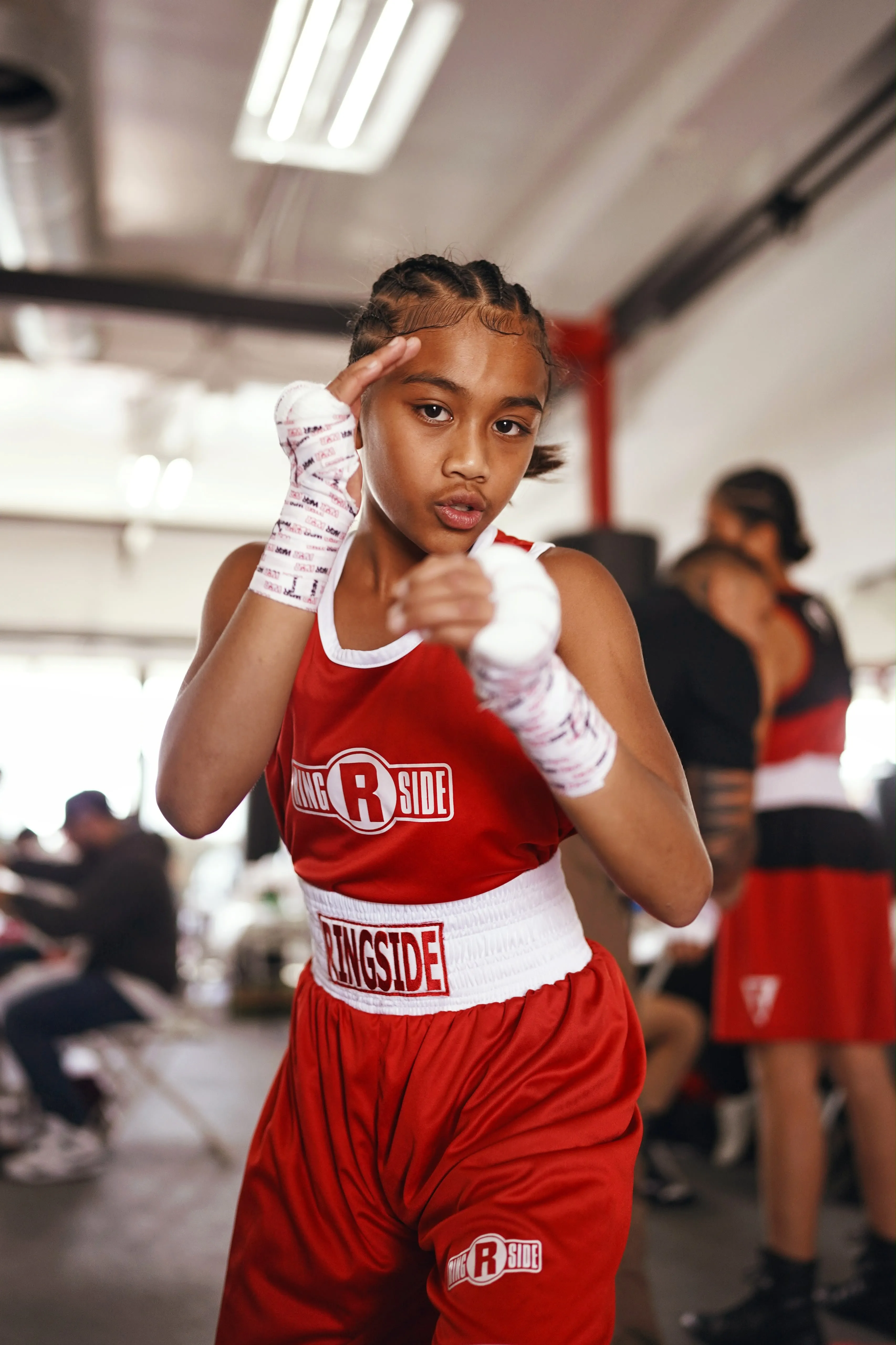 A young Iron Kingz boxer in a red team singlet with wrapped hands, in a fighting stance