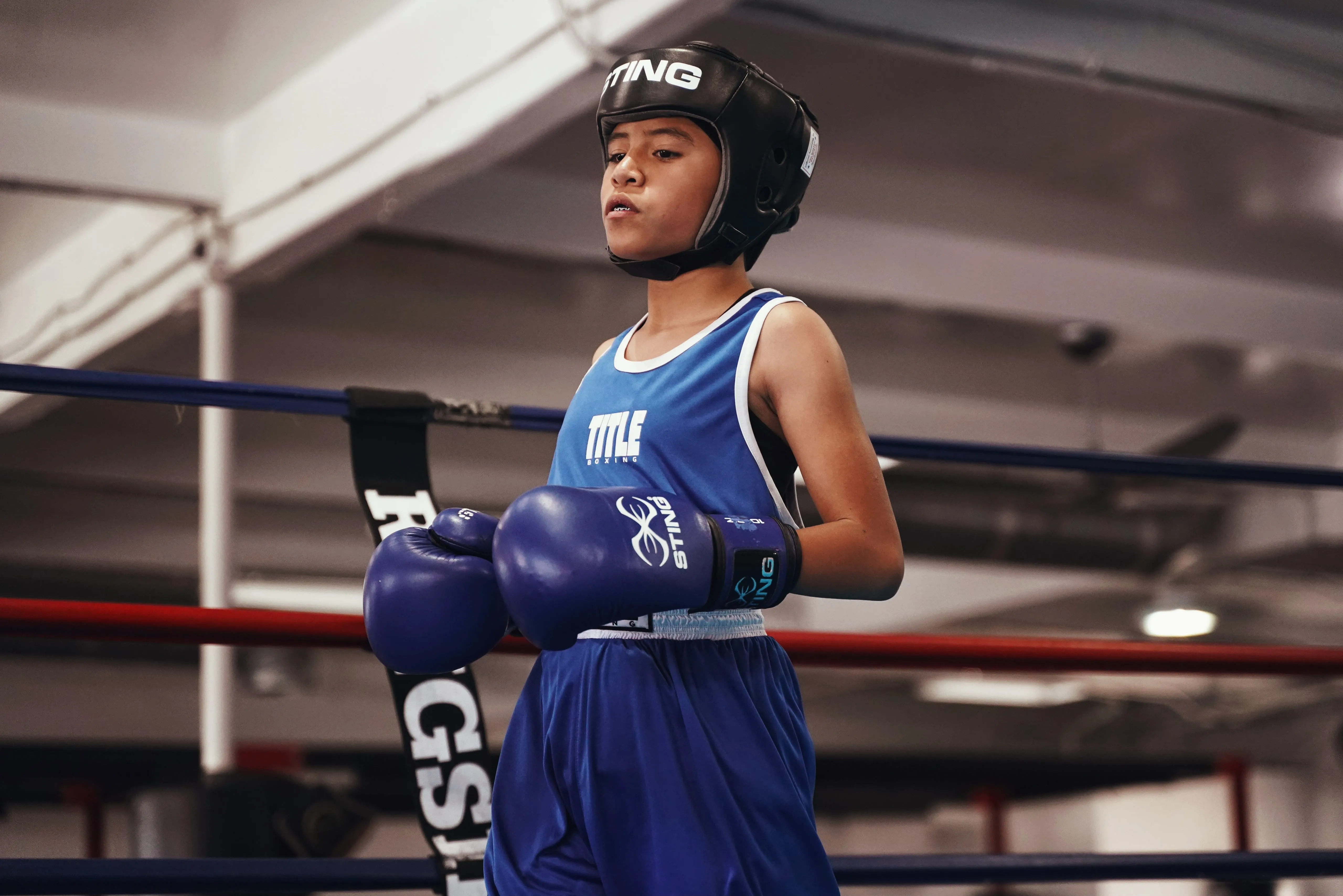 A young Iron Kingz boxer in blue gear and headgear in the corner of the ring