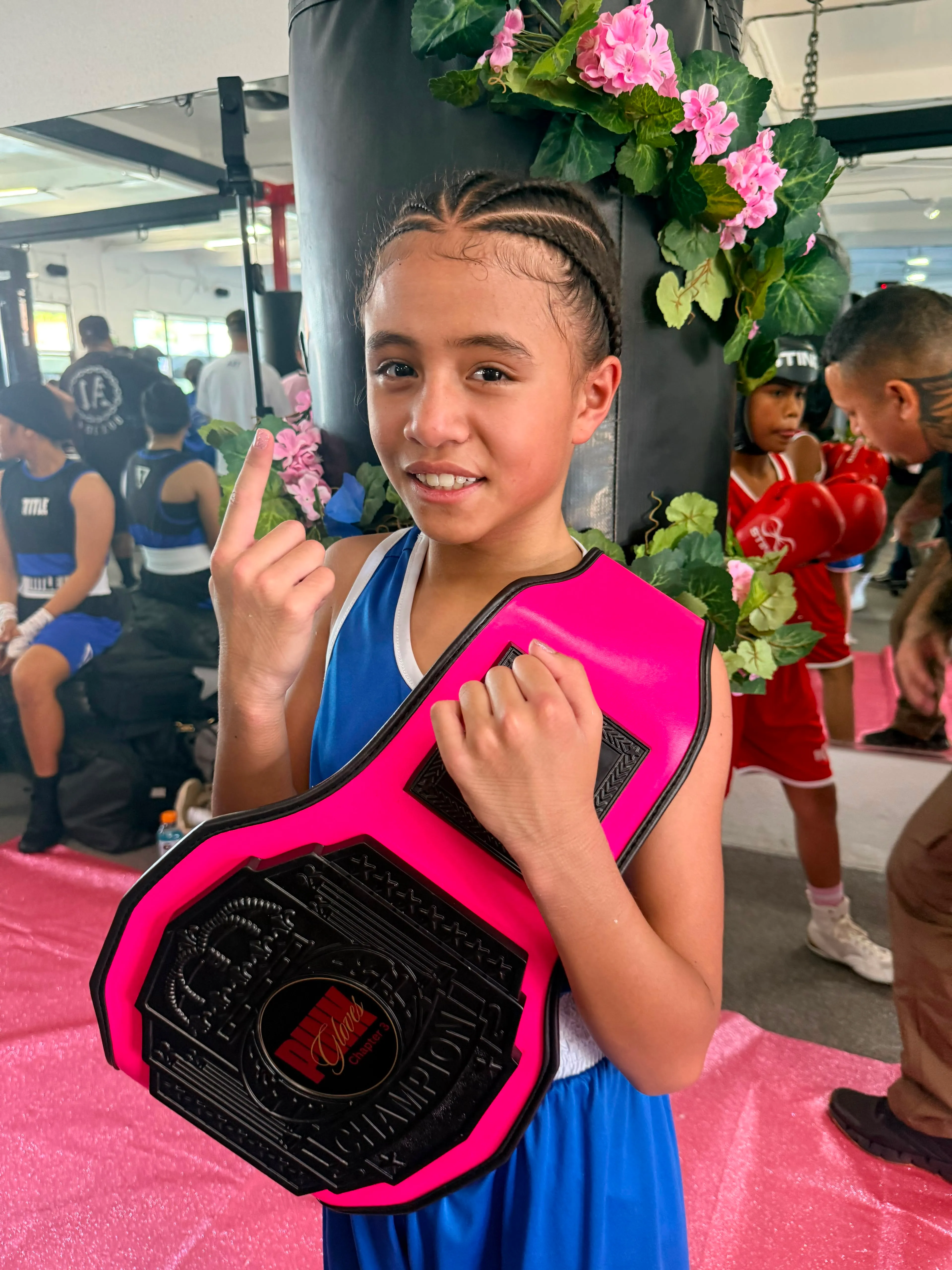 A young Iron Kingz boxer smiling and holding a championship belt