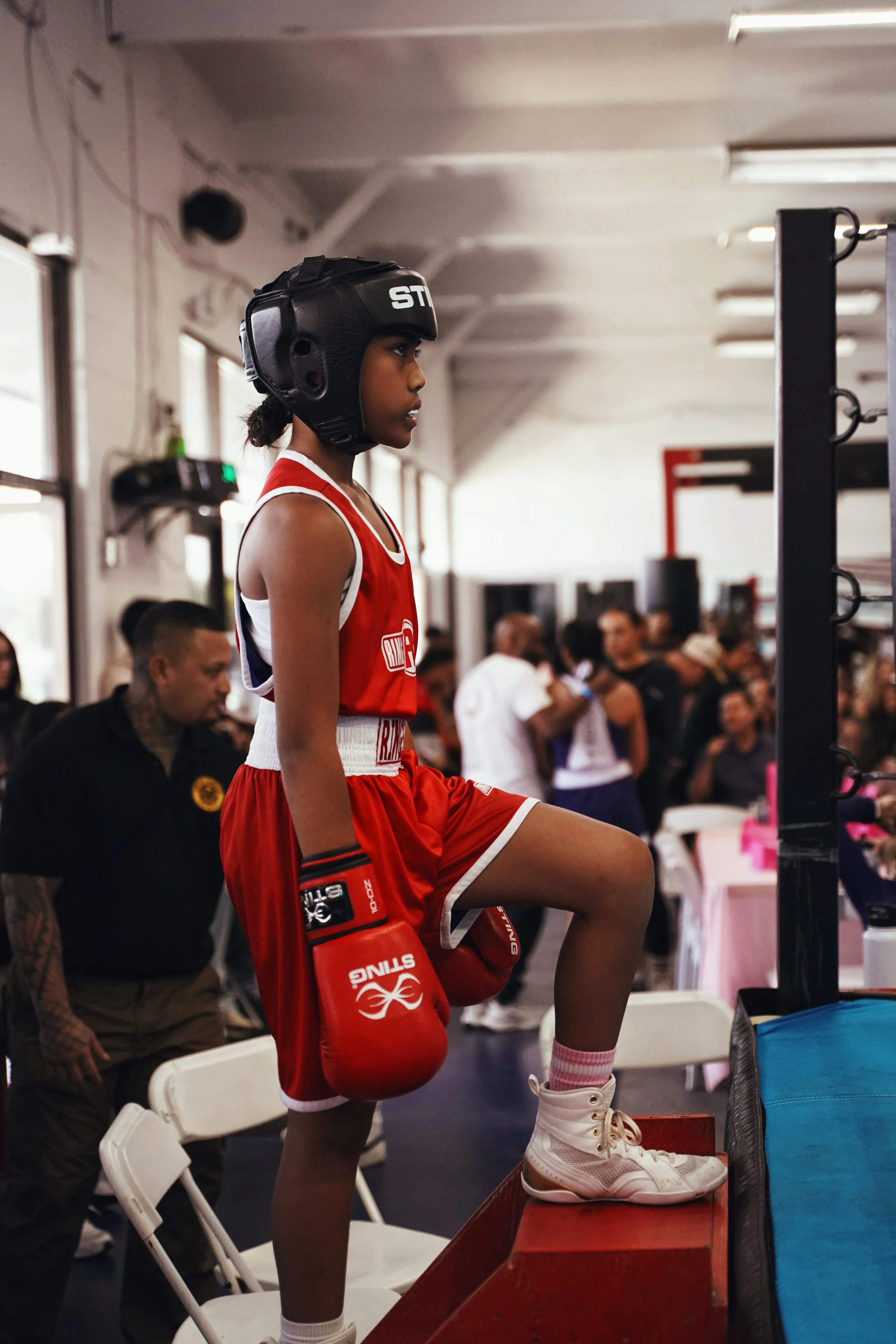 A young Iron Kingz boxer in headgear and red gear waiting ringside at a competition