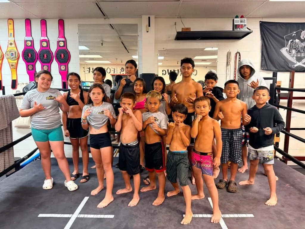 The Iron Kingz keiki team and coaches together with championship belts on the wall