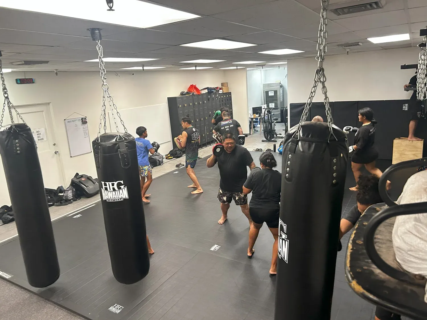Muay Thai students practicing kicks on heavy bags at Iron Kingz